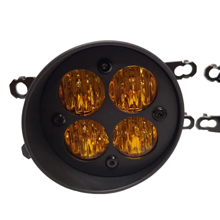 A round black vehicle light housing with four amber/yellow lensed lights, shown on a white studio background with mounting brackets partially visible on the right.