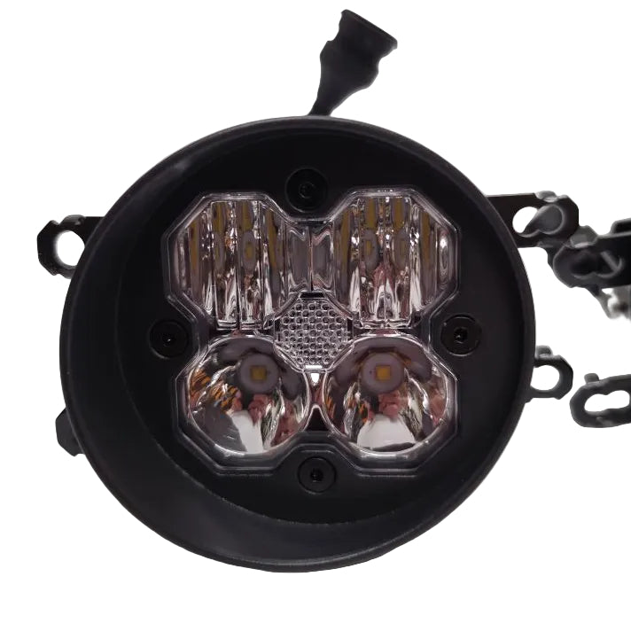 A round black automotive LED light assembly with a clear faceted lens cover, photographed on a light gray background with other parts blurred in the background.